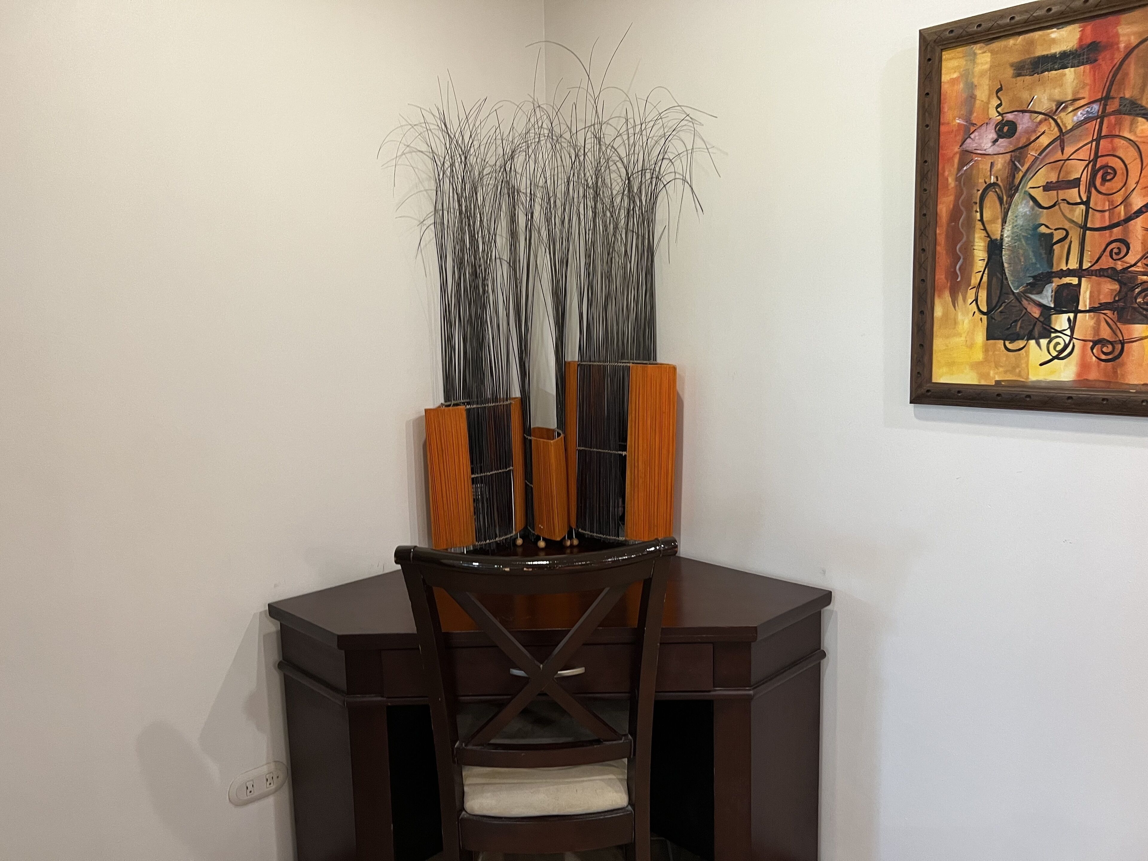 A corner dining area with a dark wooden table, a chair, and a tall vase with branches.