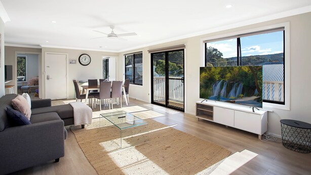 A modern living room with a sofa, TV, and dining area. - Renovated 3 bed Unit with Views (Umina Beach)