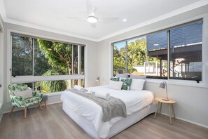 Un dormitorio moderno con una cama grande, un rincón de descanso con una silla y vistas al exterior.