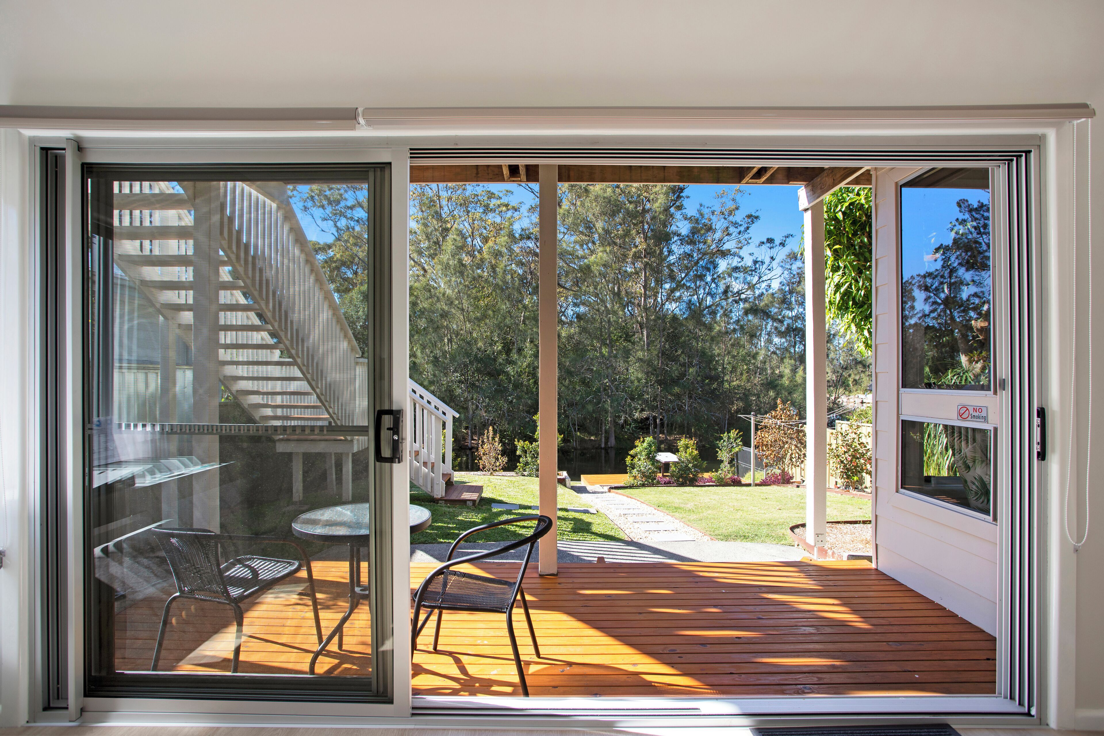 A sliding glass door leading to an outdoor deck with a wooden floor, a metal chair, and a small table.