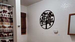 A bathroom with a toilet, a shower curtain with animal prints, a wall-mounted tree decoration, a hand dryer, and wooden cabinets.