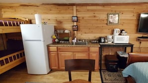 A compact kitchen with wooden cabinets, a refrigerator, a microwave, a coffee maker, and a toaster. There is a small dining area with a chair and a table.