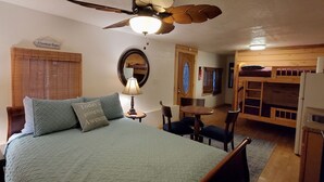 A bedroom with a bed, a ceiling fan, a mirror, a wooden bunk bed, and a small table with chairs.