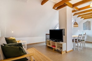 Ein modernes Wohnzimmer mit Flachbildfernseher, Essbereich mit Stühlen und Holzboden.