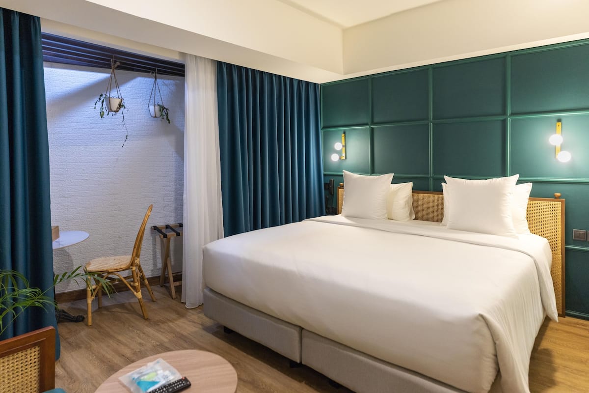 Quarto de hotel com uma cama grande, uma mesa pequena, uma cadeira e uma janela com cortinas.