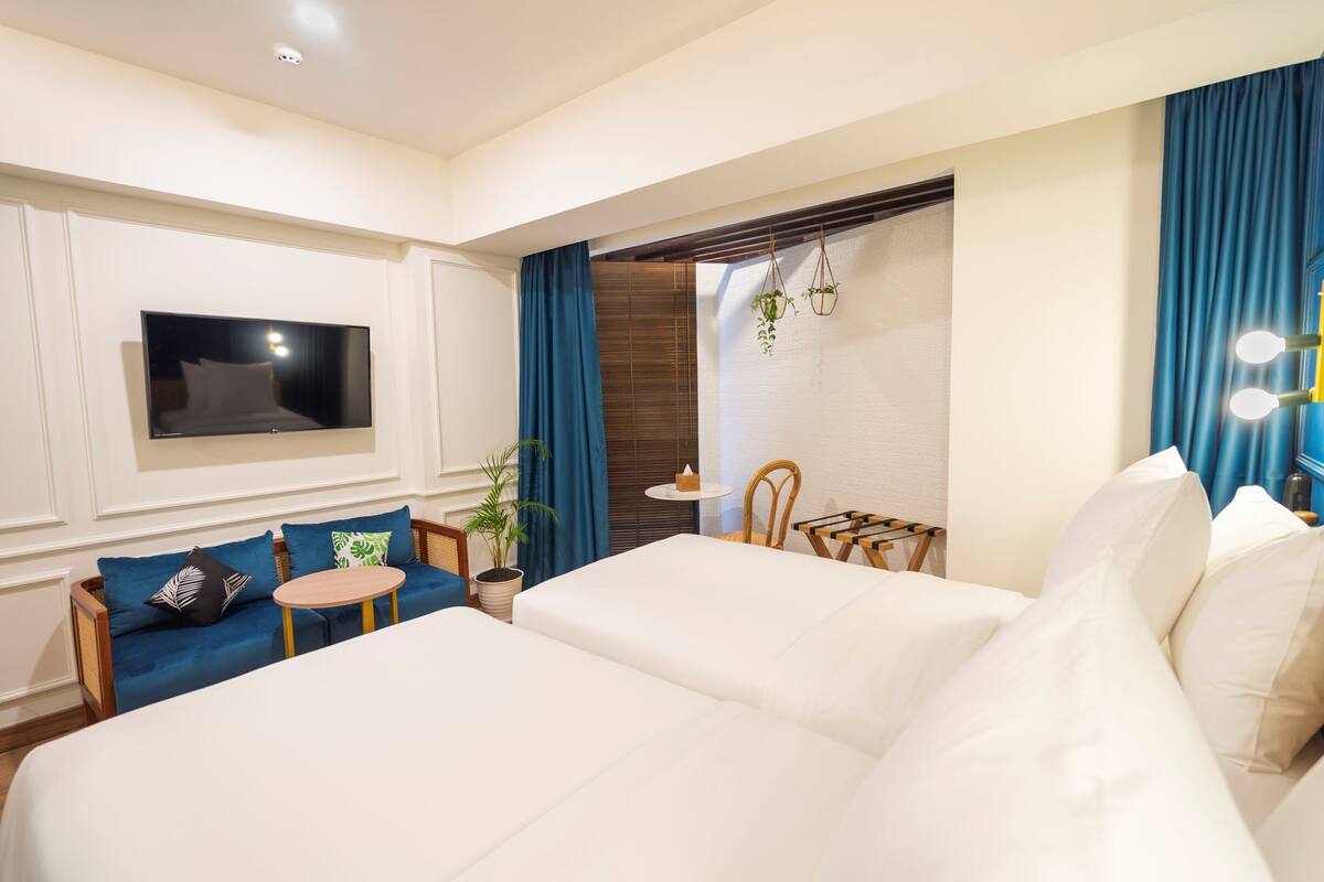 Quarto de hotel com cama grande, sofá, televisão, mesa pequena e janela com cortinas.