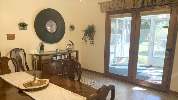 Uma sala de jantar com uma mesa grande, cadeiras, um relógio e vista para área externa por uma porta de vidro.