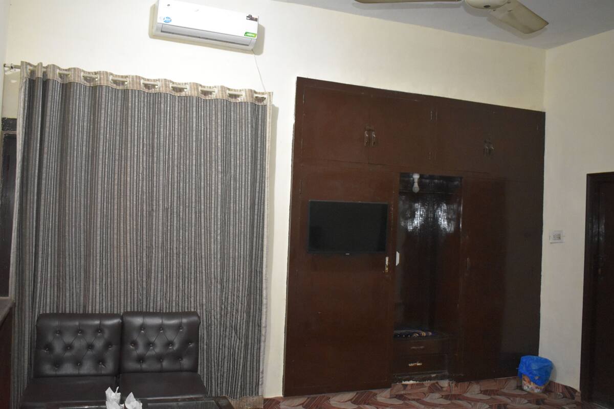 Una habitación con una puerta marrón oscuro, un televisor pequeño montado en la pared, una cortina gris y un sofá de cuero negro.