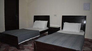 A room with two single beds, each with a wooden headboard and a grey bedspread. There is a dark wooden wardrobe on the left and a white switchboard on the wall. - Town Palace Guest House (Mekhtar)