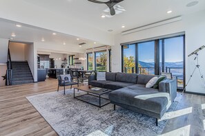 A modern living room with a gray sectional sofa, a coffee table, and a view of the outdoors through large windows.