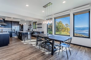 A modern kitchen with a central island, bar stools, and large windows offering scenic views.