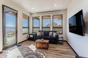 A modern living room with a large window, a flat-screen TV, and a dark-colored sofa. - Monthly Stays Available! Dog Friendly-Great Views (Steamboat Springs)