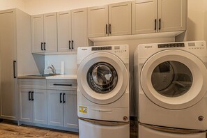 A laundry room with two Whirlpool front-loading washing machines, a countertop with a paper towel dispenser, and light-colored cabinets. - Monthly Stays Available! Dog Friendly-Great Views (Steamboat Springs)