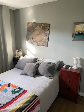 A bedroom with a bed, a nightstand, a lamp, and two paintings on the wall.