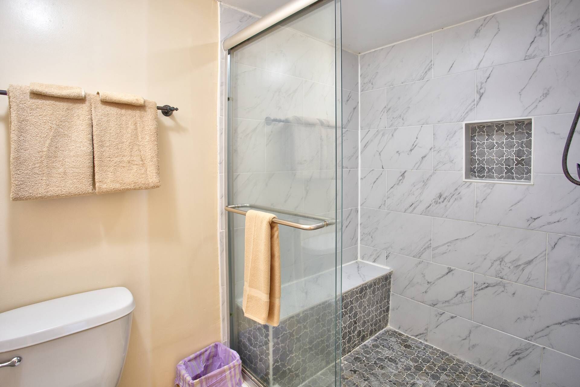 Ein Badezimmer mit Toilette, zwei Handtüchern auf einem Ablagegestell, einer Duschkabine aus Glas und Fliesenwänden.