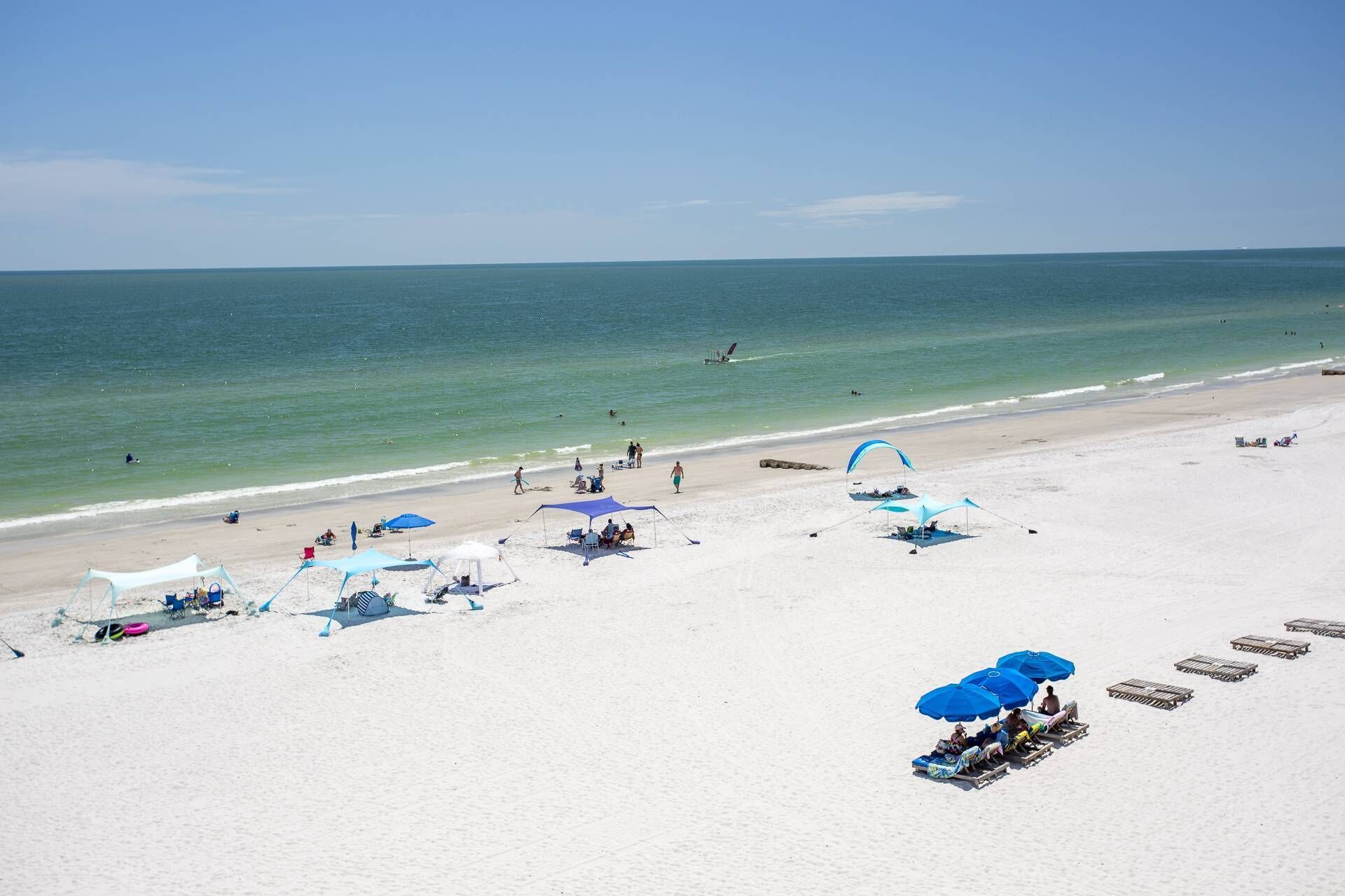 Ein Strand mit weißem Sand, klarem blauen Wasser und mehreren blauen Sonnenschirmen.