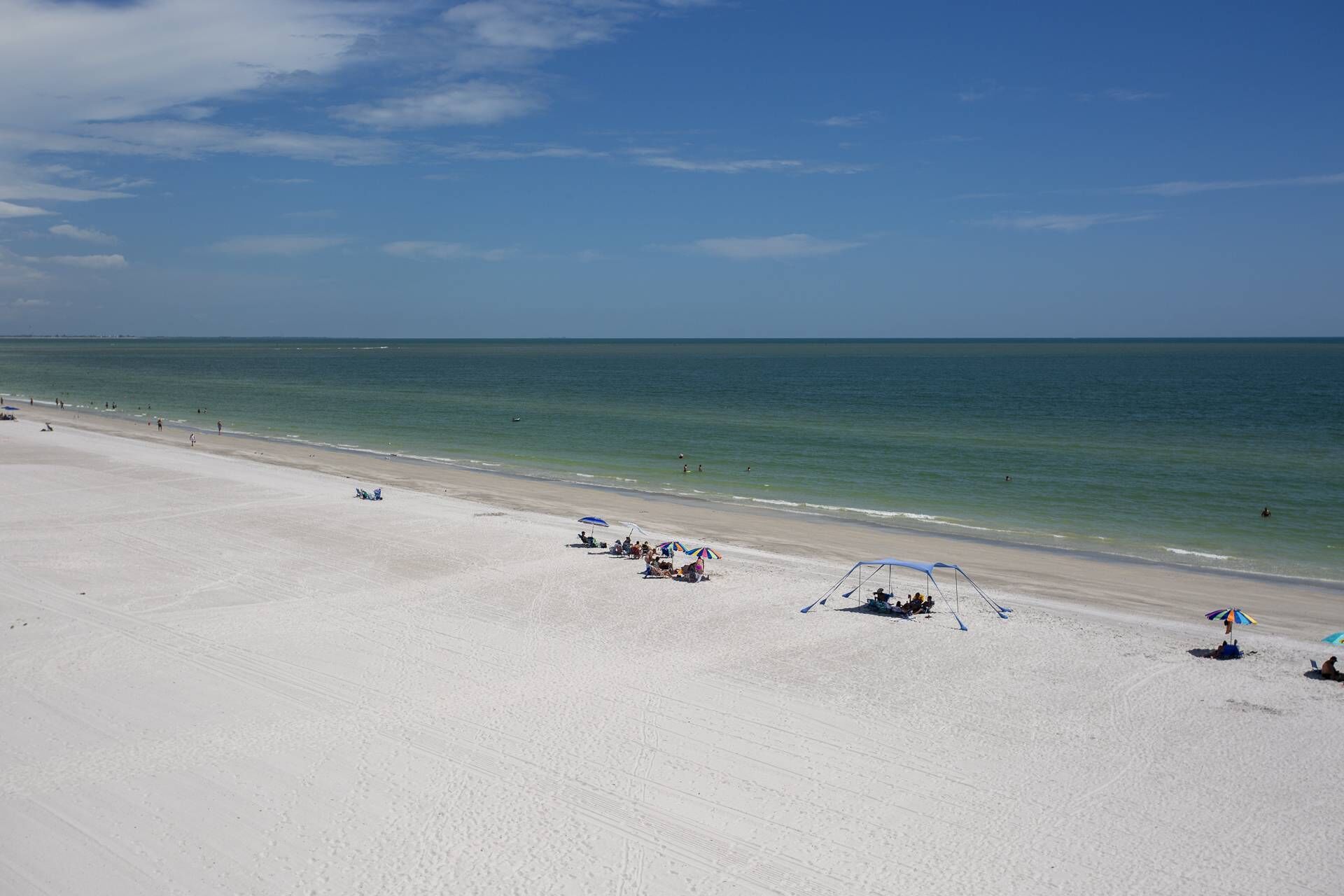 Een strand met wit zand, helderblauw water en enkele parasols.