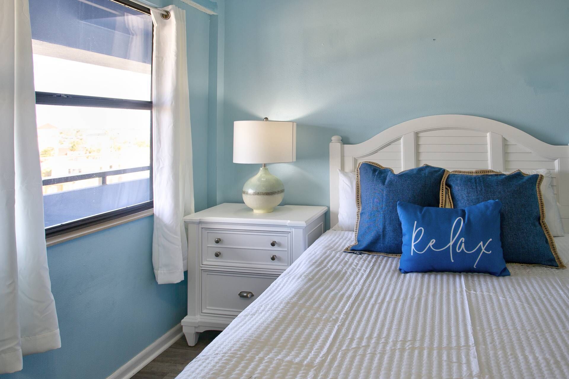 A bedroom with a bed, a nightstand, a lamp, and a window with curtains.