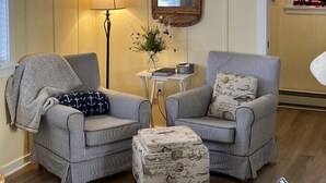 Una sala de estar acogedora con sillones a rayas, una mesita con lámpara, un espejo decorativo y un techo de madera con adornos de estrellas.