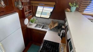 A compact kitchen with a stove, sink, and a small window. - The "Lily Pad" Boatel Houseboat (Sabula)