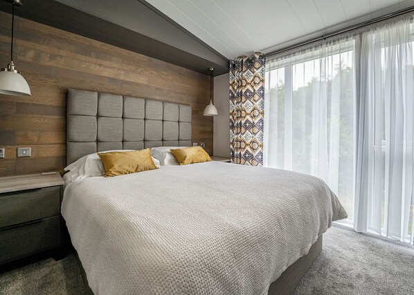 Un dormitorio moderno con una cama grande, cabecera de madera y vistas al exterior a través de cortinas translúcidas.