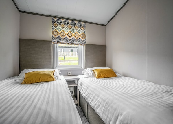 Quarto com duas camas, uma janela com cortina estampada e vista para uma área gramada.