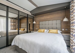 Un dormitorio moderno con una cama grande, mesitas de noche, un espejo y un aplique de techo.