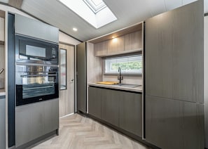 Cozinha moderna com eletrodomésticos embutidos, janela com persianas e chão com padrão herringbone.