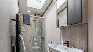 Un bagno moderno con box doccia in vetro, un water, un lavandino con specchio sopra e un porta asciugamani.