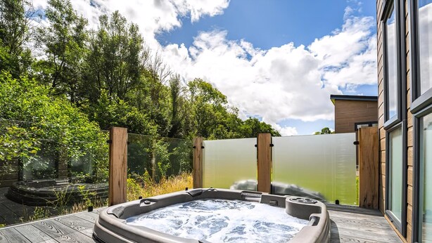 Un bain à remous sur une terrasse en bois, avec vue sur les arbres et un bâtiment en arrière-plan.