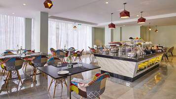 A modern hotel dining area with a central buffet, colorful chairs, and pendant lighting.