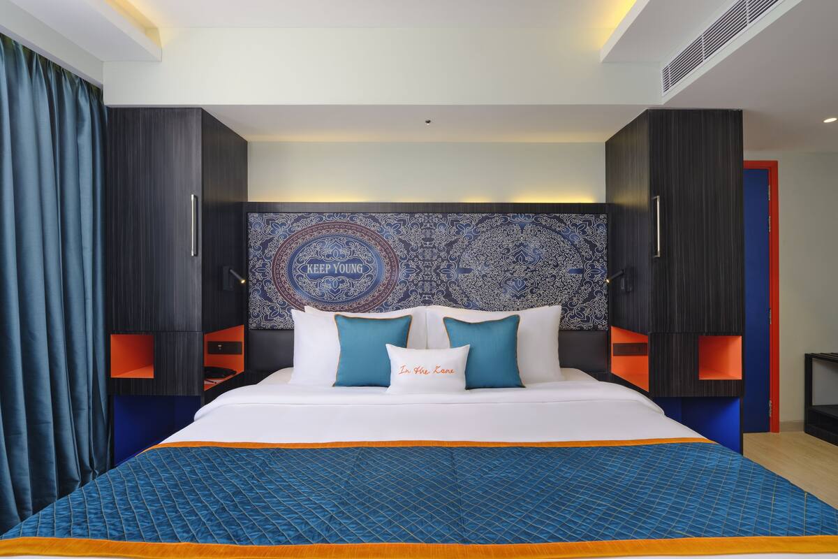 A modern hotel room with a large bed, a patterned headboard, and a blue accent wall.