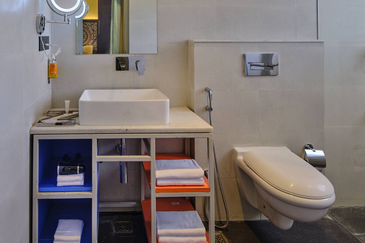 A modern bathroom with a white sink, two wall-mounted lights, a round mirror, and a toilet.