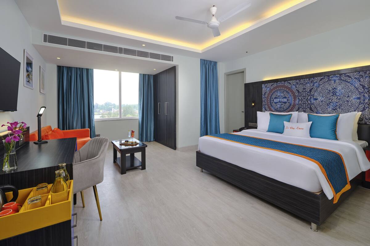 A hotel room with a bed, desk, chair, and a view of the outdoors.