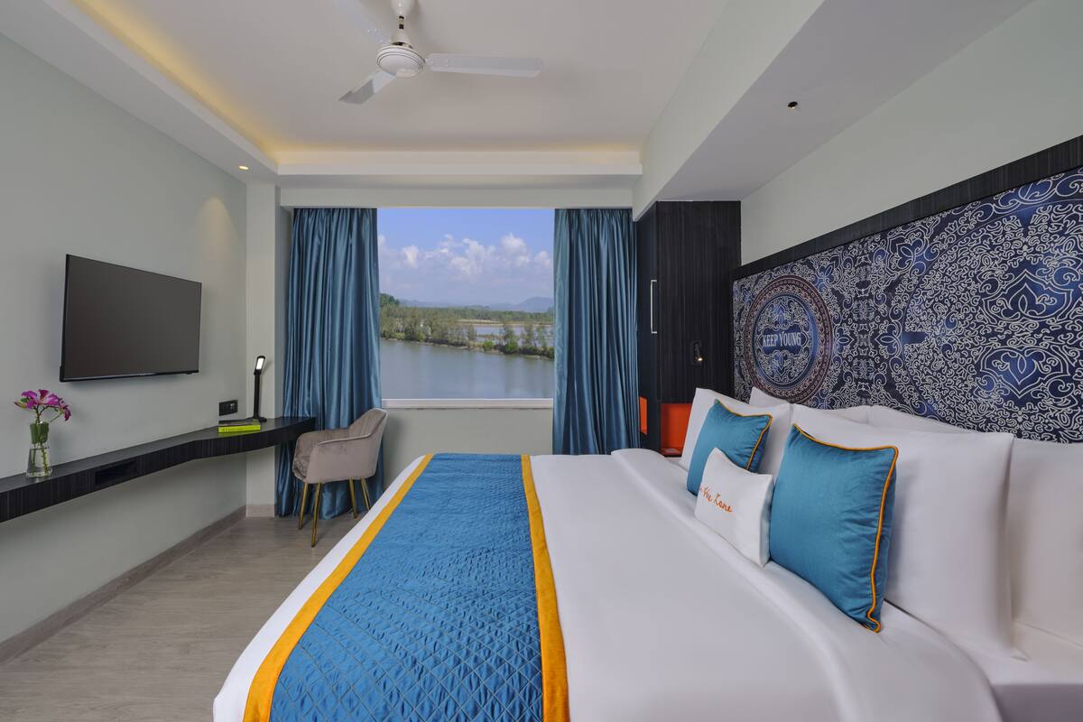 A modern hotel room with a large bed, a desk, a chair, and a TV.