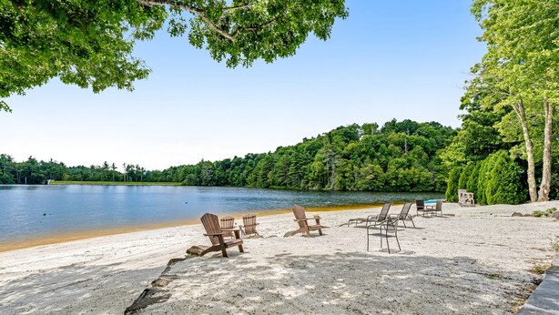 Una playa junto al lago con sillas Adirondack y una mesa, rodeada de un bosque denso.
