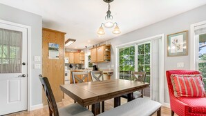 Un comedor con una mesa y sillas de madera, una silla tapizada de rojo y vistas a través de ventanas amplias.