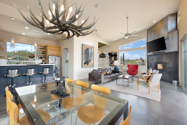 A spacious living area with a glass dining table, comfortable seating, a fireplace, and a large TV.