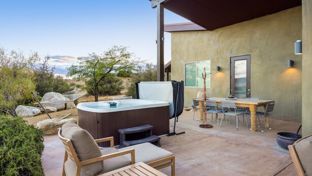 Een terras buiten met een jacuzzi, houten meubels en een eettafel.