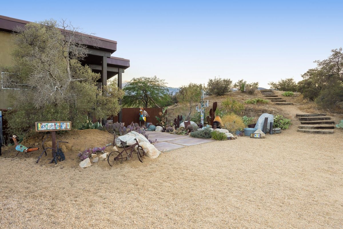 A building with a covered porch, a gravel driveway, and a staircase leading up a hill.