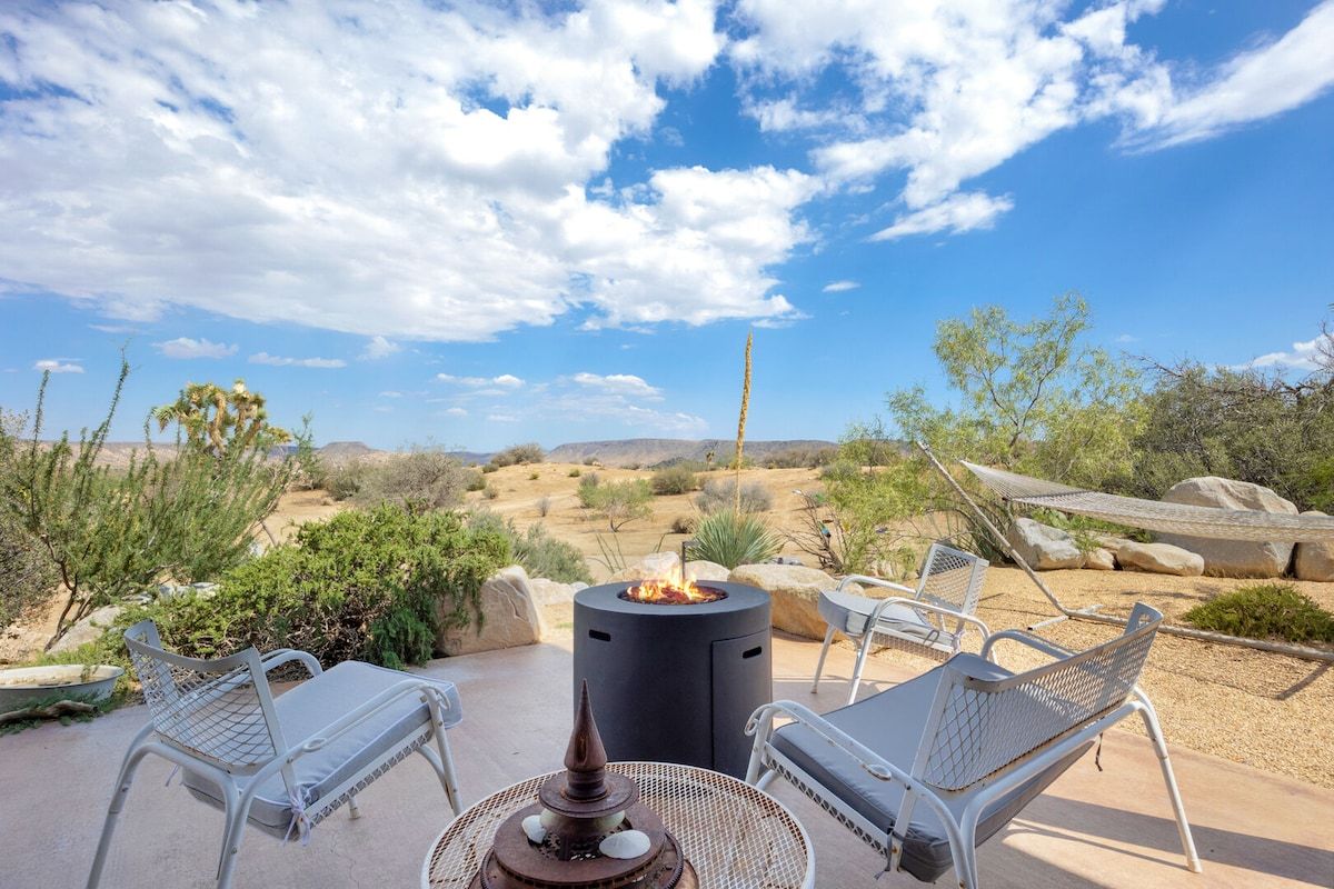 Un patio al aire libre con un hogar para fuego, dos sillones de lounge y vistas a un paisaje desértico.