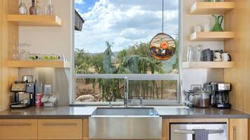 A kitchen with a large window, stainless steel appliances, and wooden shelves.