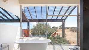 Een moderne badkamer met een vrijstaand bad, grote ramen en uitzicht op een woestijnlandschap.