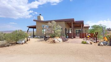 A modern house with a large patio, surrounded by desert vegetation and a clear sky.