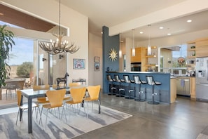 A modern kitchen with a bar area, dining space, and a large window. - Jackalope Junction-Hot Tub Fire Pit BBQ Views (Pioneertown)
