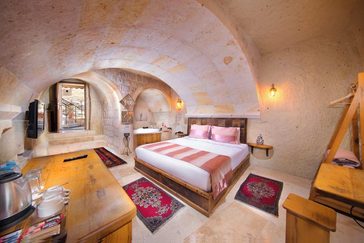 A bedroom with a stone ceiling, a wooden bed, a small table, and a window.