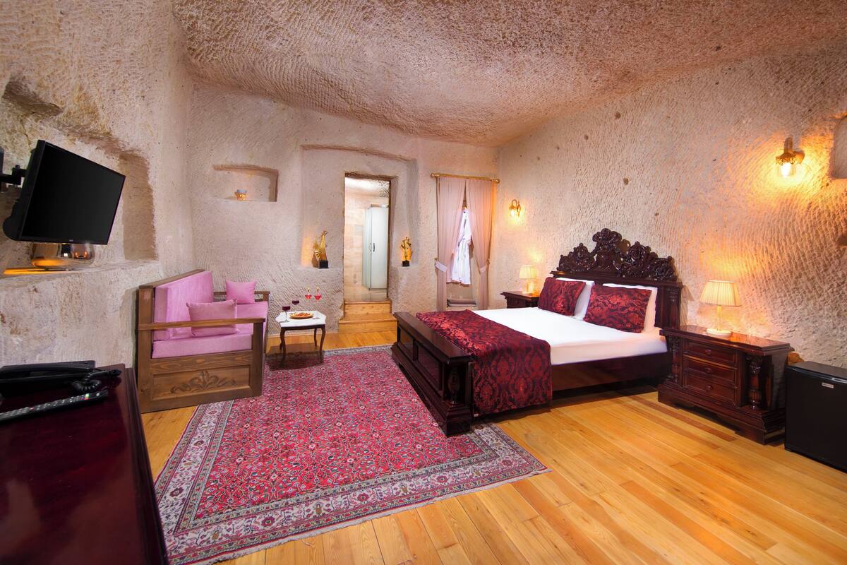 A bedroom with a wooden bed, a desk, a chair, a television, and a red rug.