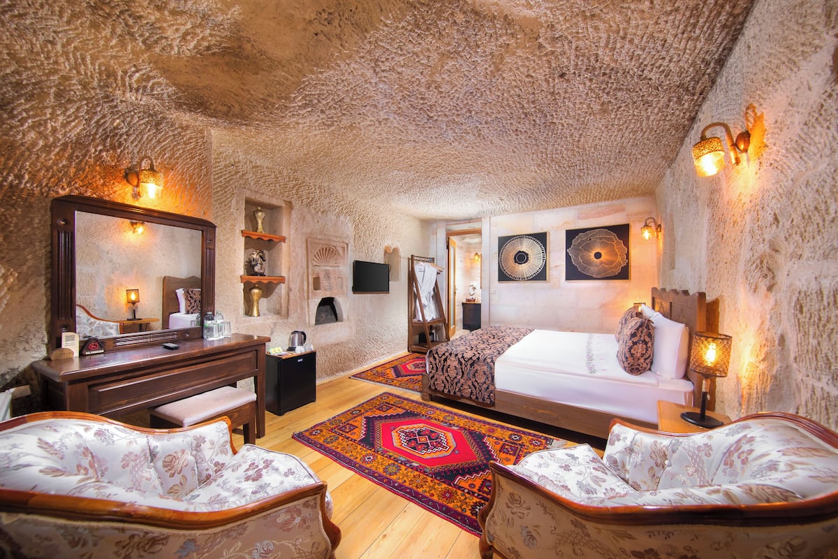 A bedroom with a wooden bed, a desk, a chair, a dresser, and a large mirror.