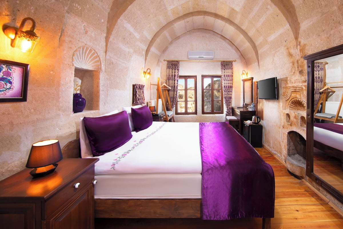 A bedroom with a large bed, wooden furniture, and a stone wall.