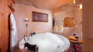 Une salle de bain avec une grande baignoire, une étagère en bois sur laquelle est posée une serviette, une bougie fixée au mur et une petite table avec une assiette et des verres.